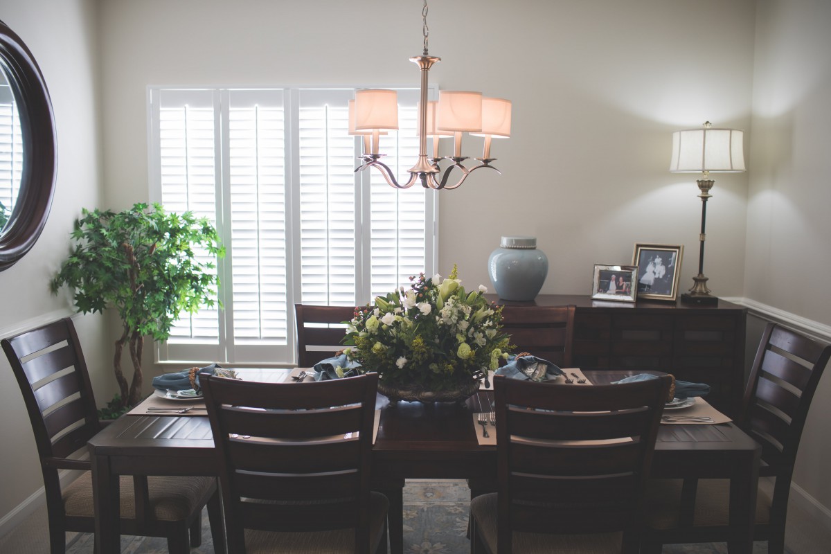 A cozy dining room with a central table adorned with flowers and surrounded by chairs, illuminated by a chandelier.