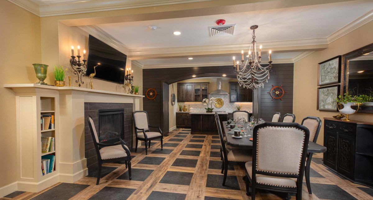 A stylish dining room with a chandelier, fireplace, and a view into the kitchen.