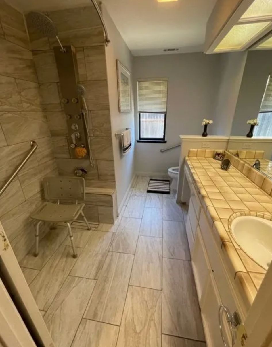 A bathroom with a shower, sink, and tiled flooring.