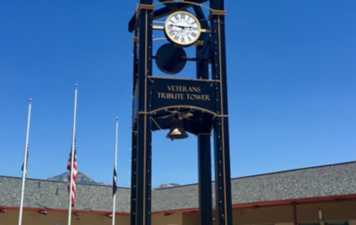 A clock tower at a veterans memorial site with flags in the background.