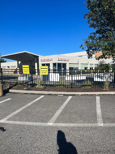 A view of a fenced building with visible signs in a parking lot under a clear blue sky.