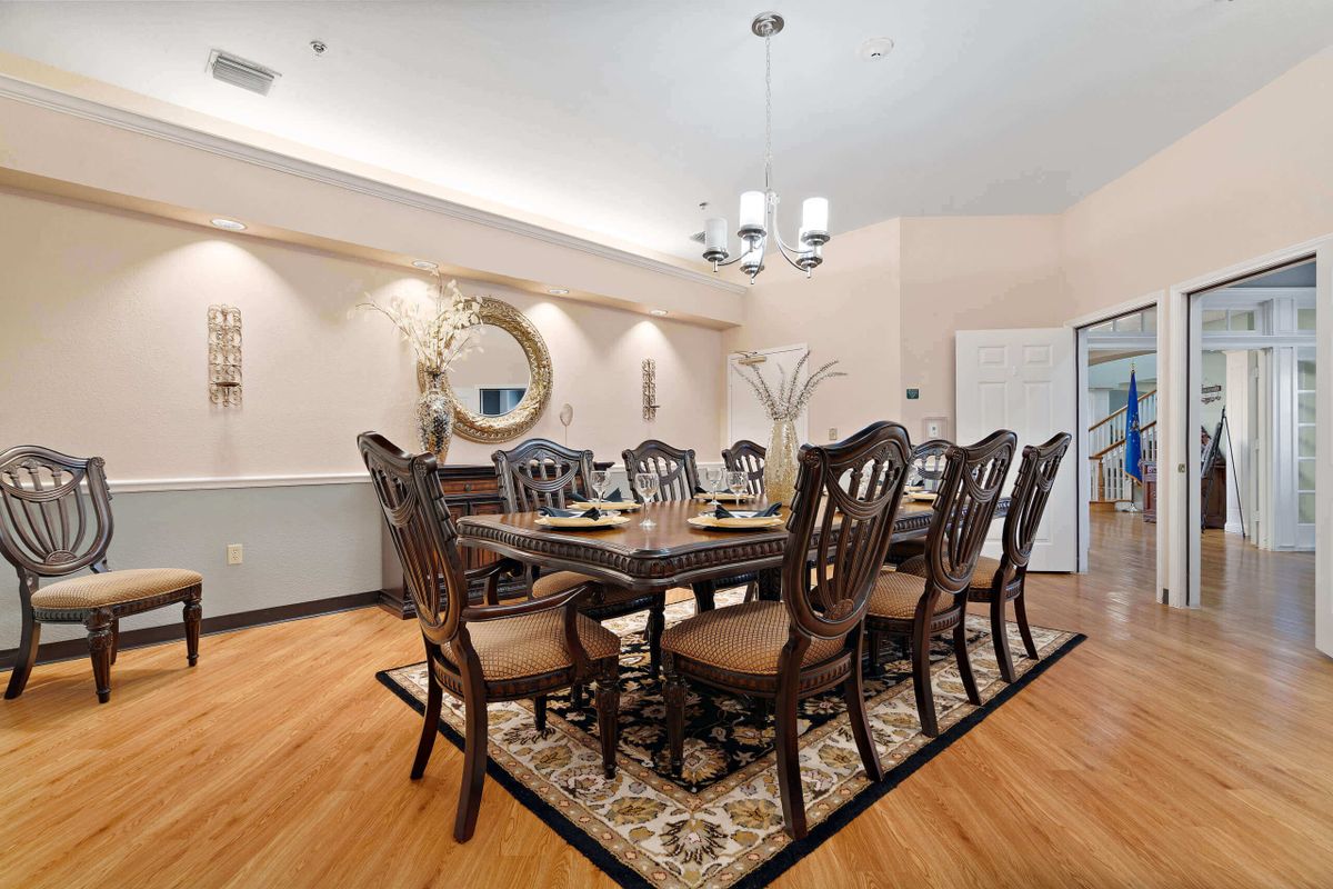 A well-appointed dining room featuring a large wooden table with intricately designed chairs, an elegant chandelier, and a decorative mirror on the wall.