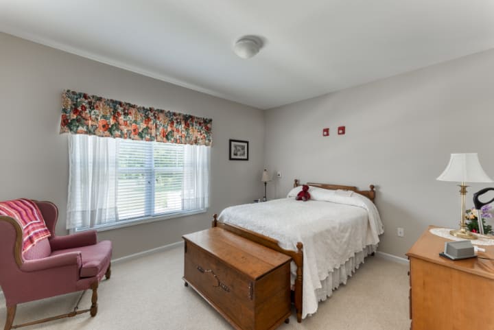 A cozy bedroom with a wooden bed, chest, and a window with floral curtains.
