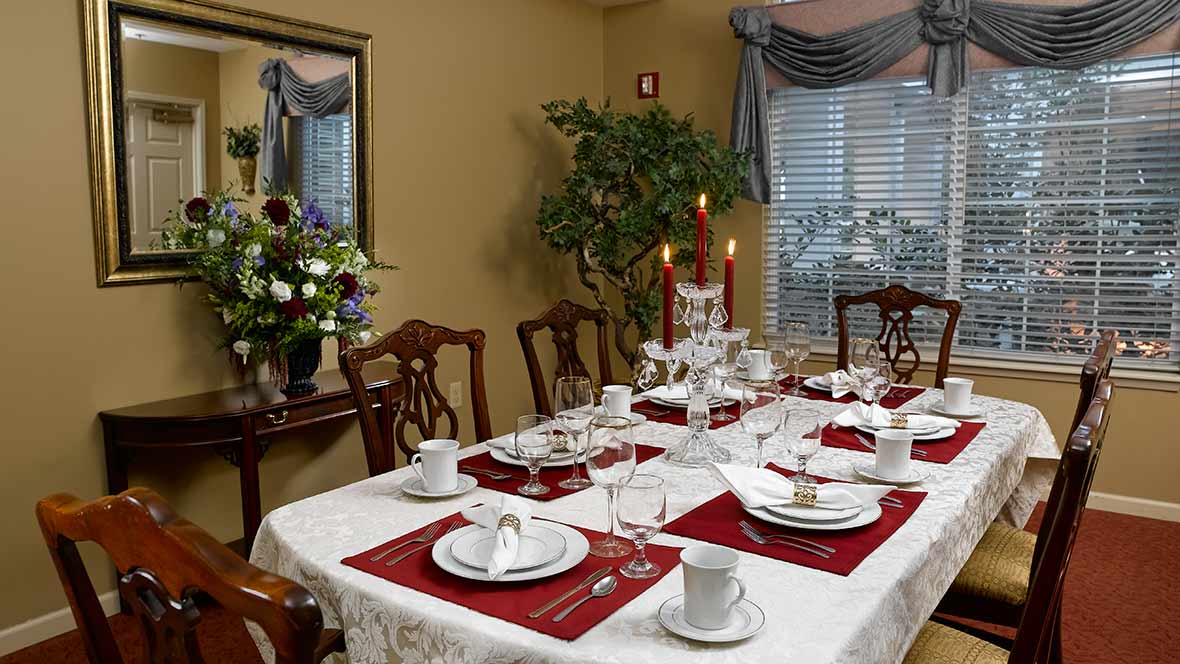 A formal dining room adorned with an elegant table setting, featuring red placemats, white dinnerware, and lit candles.