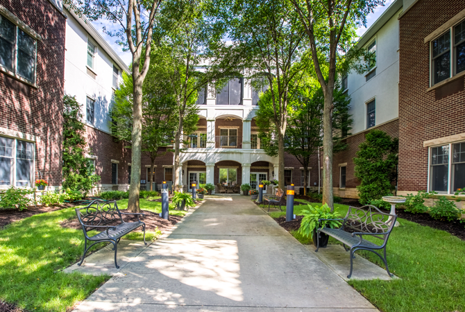 A peaceful courtyard with benches and trees in front of a residential building.