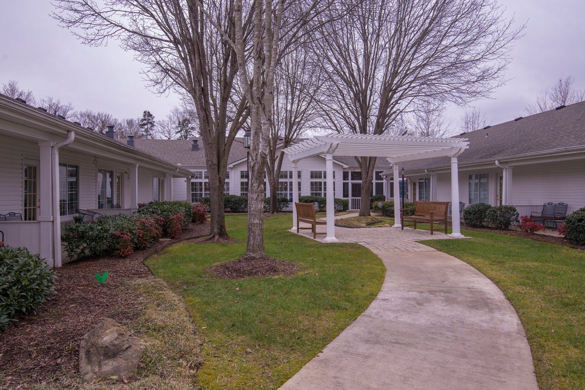 A peaceful courtyard with a winding walkway and a pergola surrounded by trees and benches.