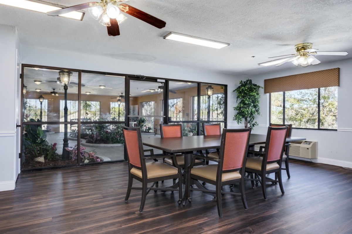 A spacious dining area with a wooden table, cushioned chairs, and large windows overlooking greenery.