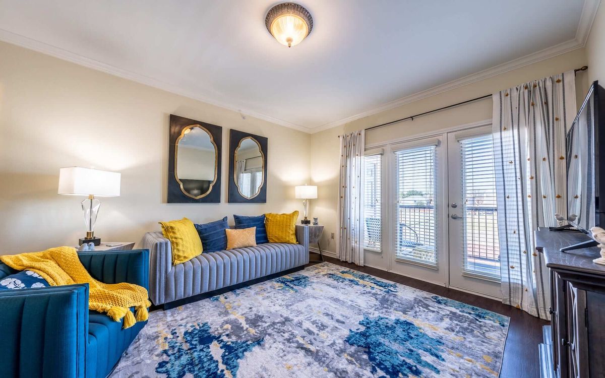 A stylish living room with a blue and yellow color scheme, featuring a striped sofa, decorative mirrors, and large French doors.