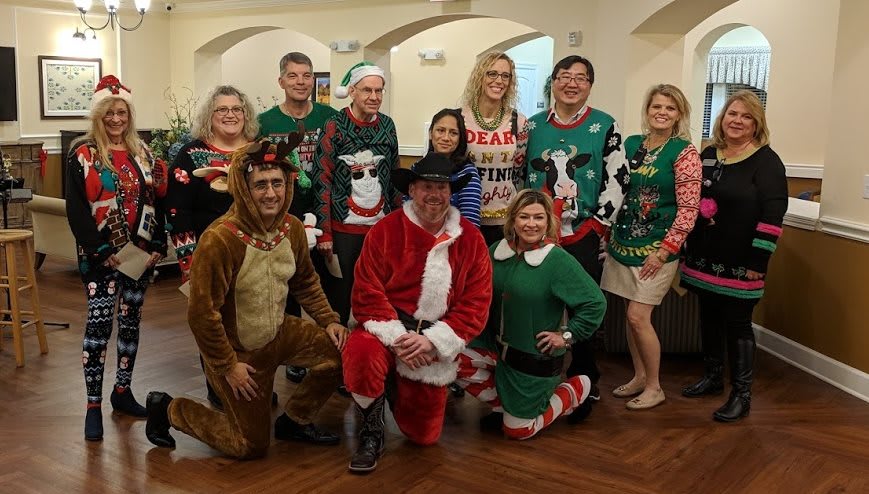 A group of people dressed in festive Christmas costumes, including Santa, elves, and reindeer, posing together indoors.