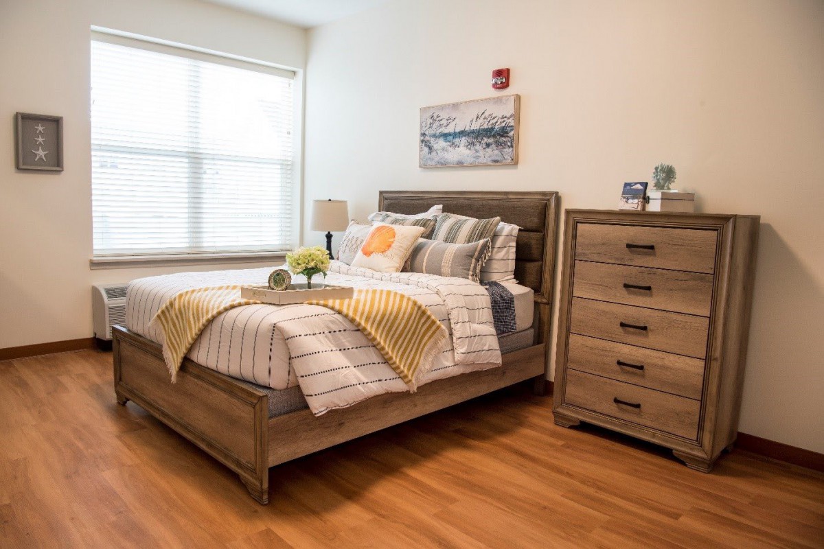 A cozy and modern bedroom featuring a wooden bed frame, dresser, and natural lighting.