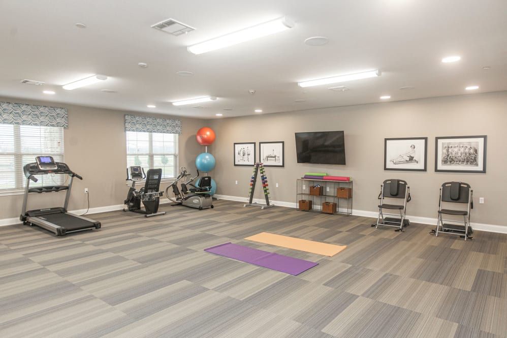 A well-lit exercise room with fitness equipment, including yoga mats, a treadmill, stationary bike, and exercise balls.