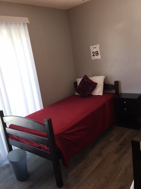 A minimalist bedroom featuring a single bed with red bedding, complemented by a nightstand.