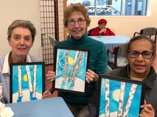 A group of women proudly display their artwork during an art class.