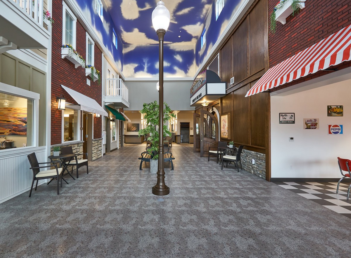 An indoor hallway designed to resemble an outdoor street, featuring street lamps, shopfronts, and a painted sky ceiling.