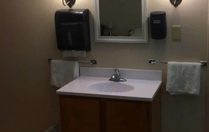 A bathroom with a sink and mirror, featuring towel and soap dispensers.