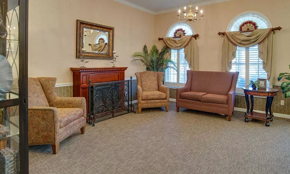 A traditional living room with cozy seating around a fireplace, featuring armchairs, a sofa, and a chandelier.