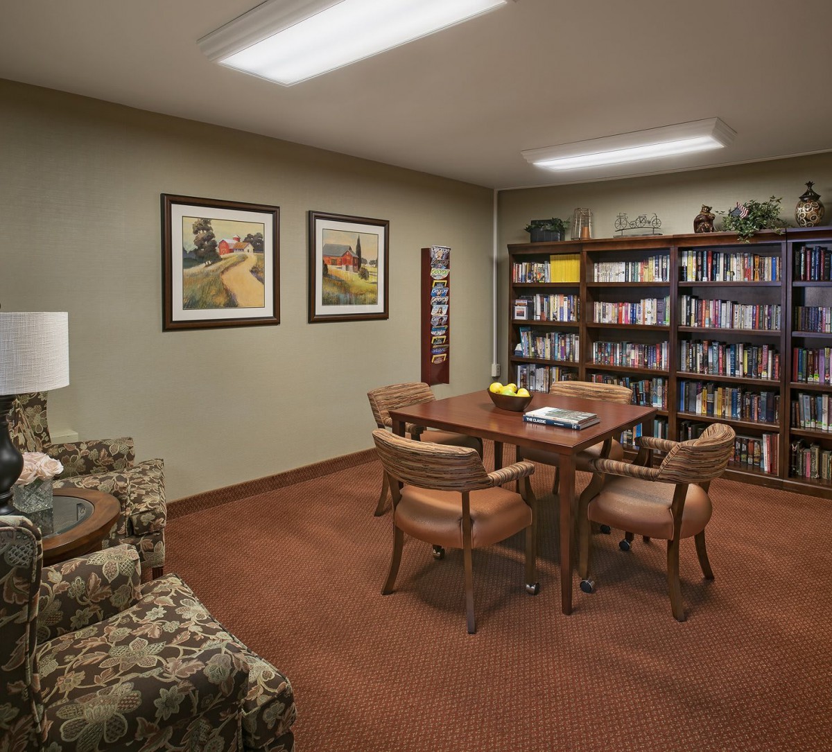 A cozy reading room with a table, chairs, and a bookshelf filled with books.