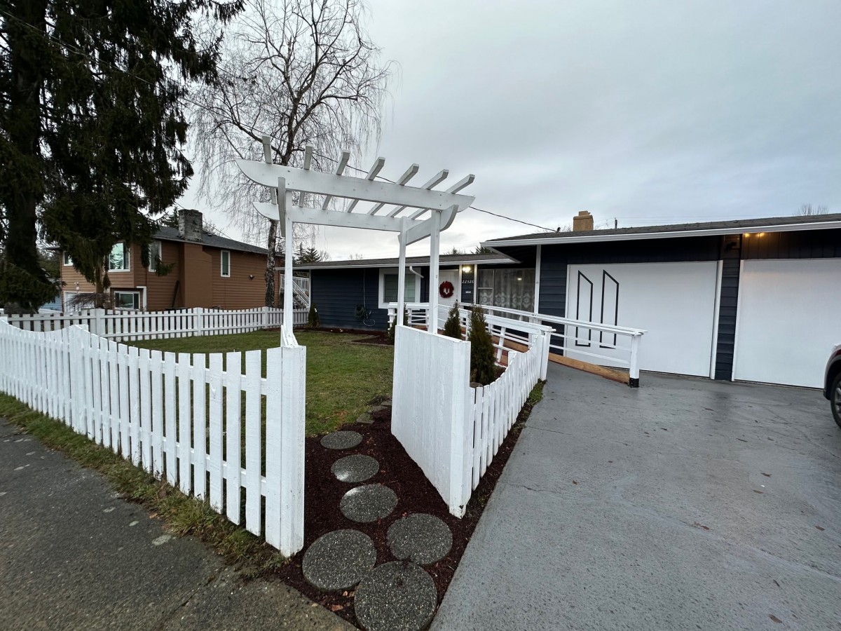 A suburban house with a white fence and pergola in the front yard.