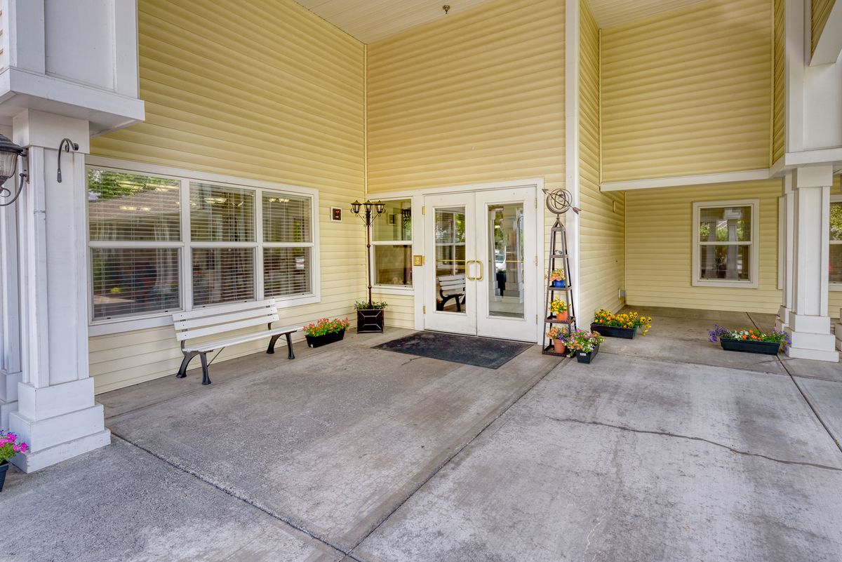 The entrance of a building with glass doors, yellow siding, and a bench.