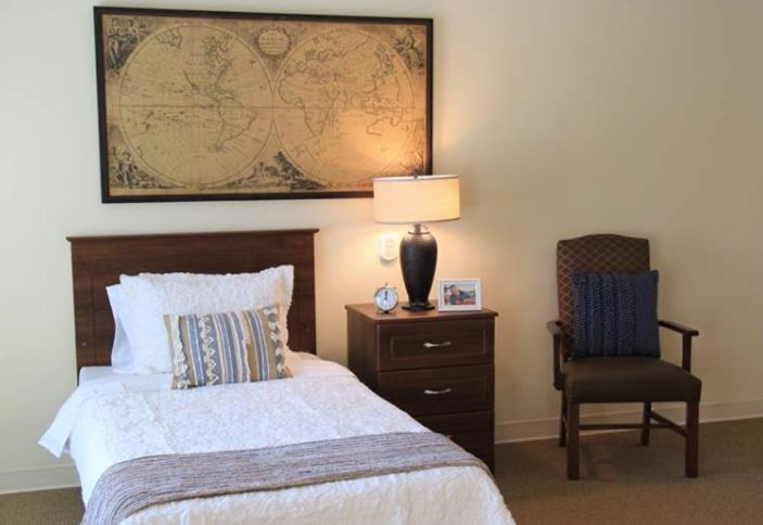 A cozy bedroom with a bed, nightstand, lamp, and map wall art.