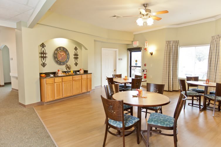 A cozy dining area with round tables and cushioned chairs, featuring a decorative wall and ceiling fan.