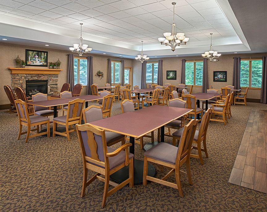 A spacious dining room featuring several tables and chairs, with chandeliers, a fireplace, and large windows.
