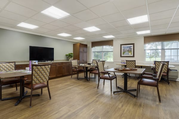 A well-lit dining area with several tables and chairs, featuring a television and large windows.