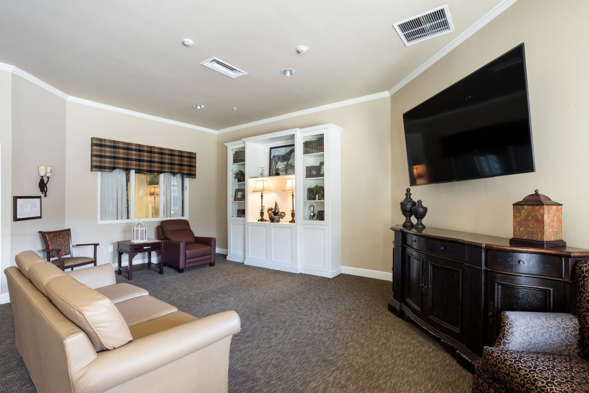A cozy living room with a large television, comfortable seating, and decorative shelves.