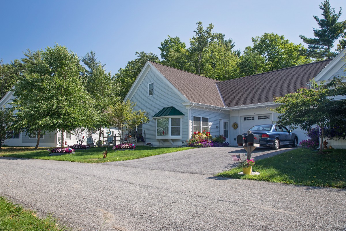 A suburban house with a driveway and a parked car, surrounded by trees and a well-kept lawn.