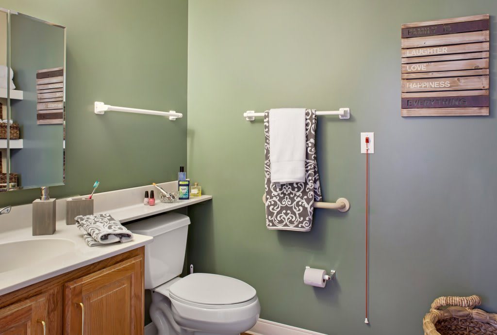 A neatly arranged bathroom with green walls, featuring a toilet, sink, and towel rack.