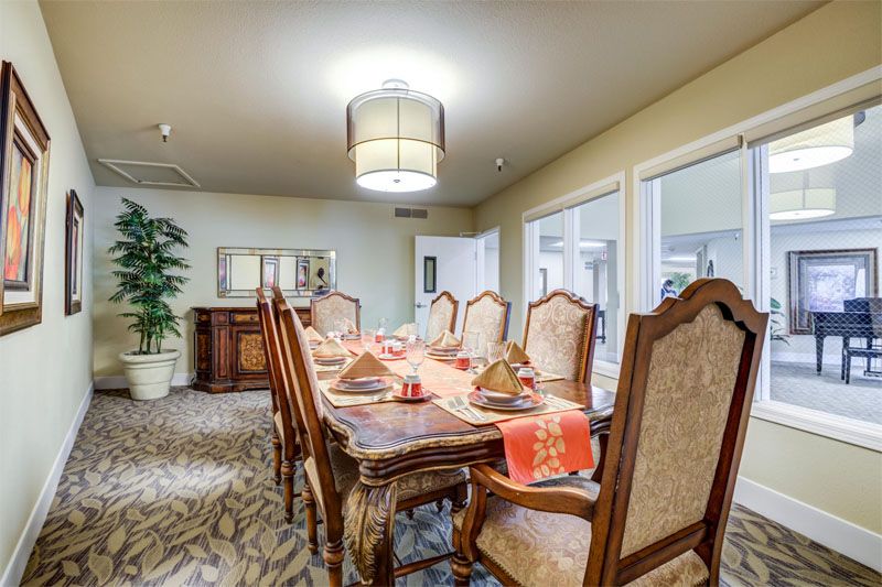 A well-appointed dining room featuring a long wooden table set for a meal, surrounded by ornate chairs and illuminated by a modern chandelier.