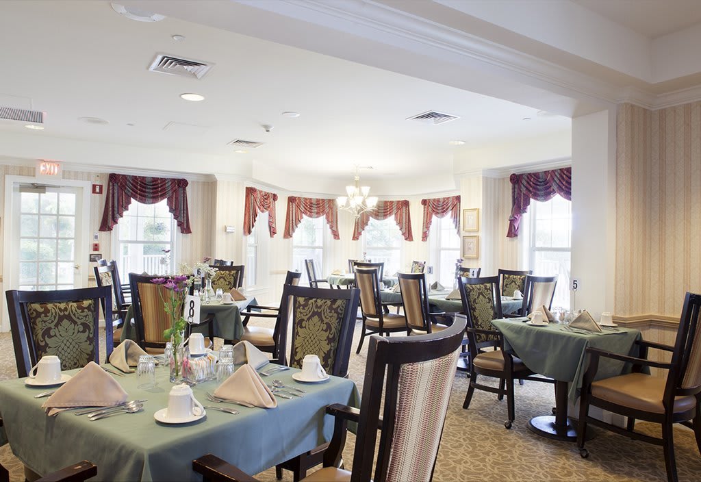 An elegantly set dining area with tables and chairs, featuring large windows adorned with red curtains.
