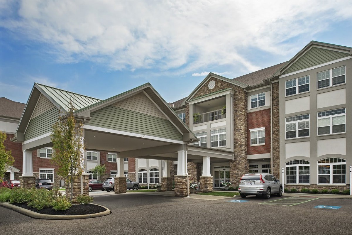 A view of a multi-story residential building with a covered entrance and parked cars.