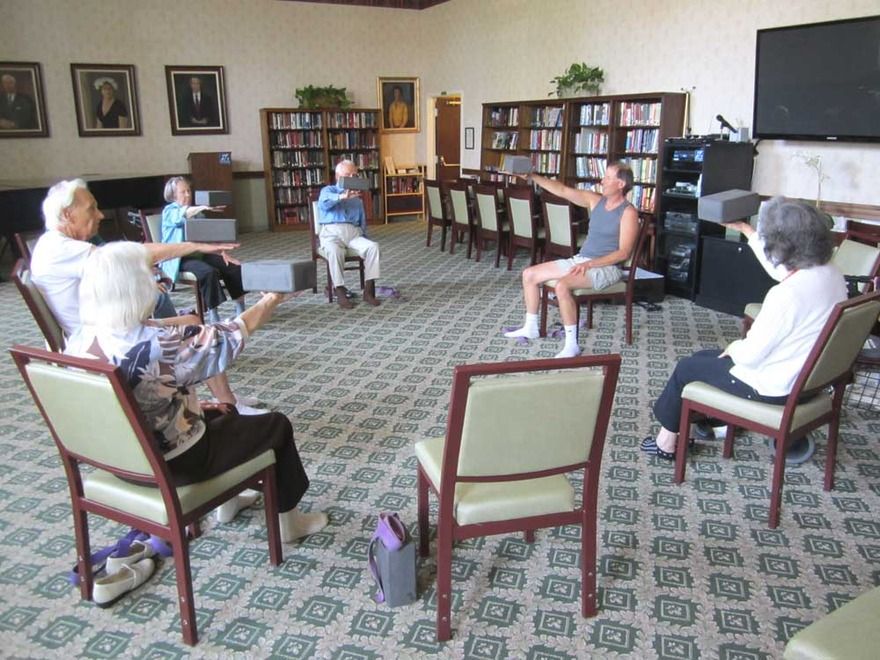 A group of seniors participating in a chair exercise class in a library setting.