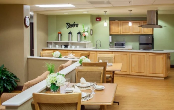 A cozy dining area with neatly set tables and a kitchen in the background.