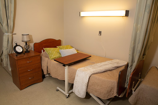 A simple hospital room with a bed, a nightstand, and a lamp, designed for patient comfort.