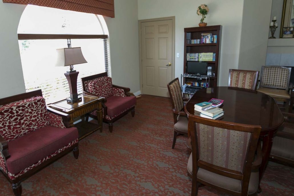 A cozy office space with a bookshelf, chairs, and a table by the window.