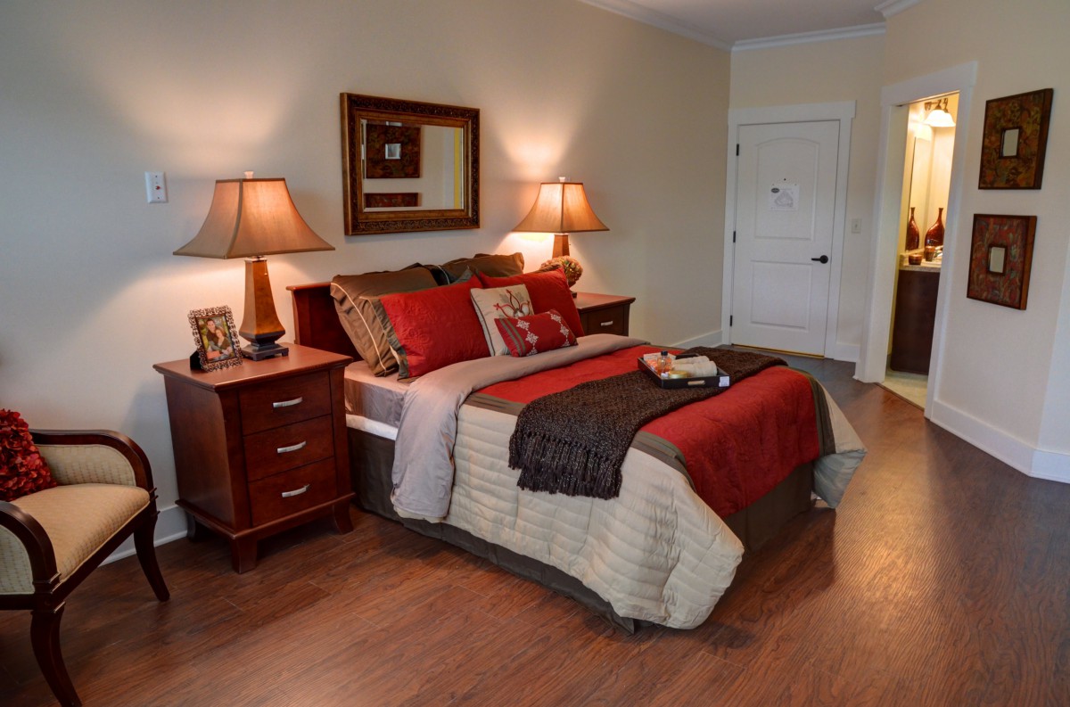 A cozy bedroom with elegant decor, featuring a bed with red and beige bedding, wooden nightstands, and warm lighting from matching lamps.