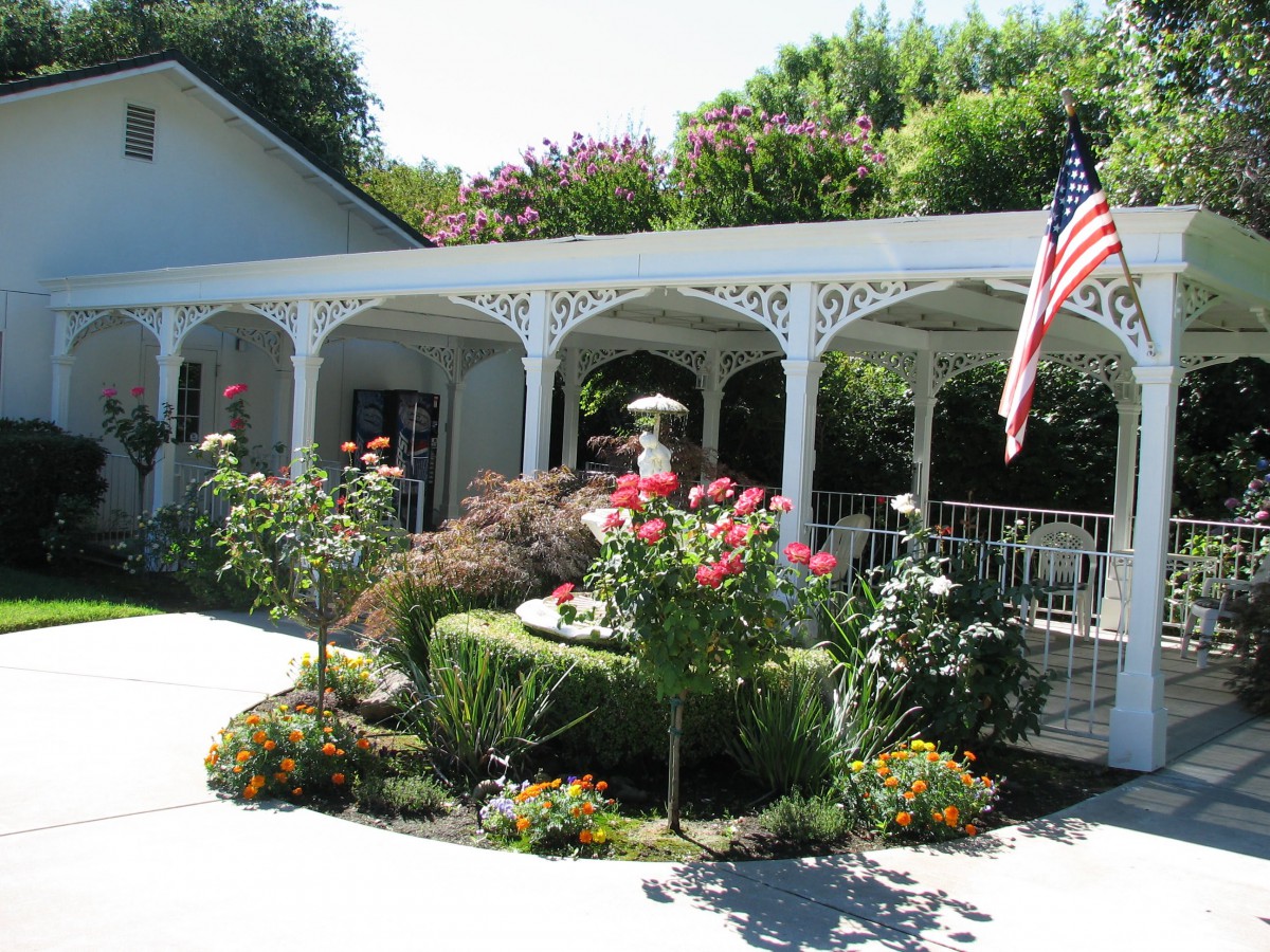 A charming garden with colorful flowers and a white veranda, adorned with an American flag.