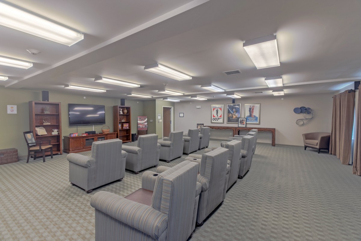 A well-lit waiting room with rows of comfortable chairs and a television.