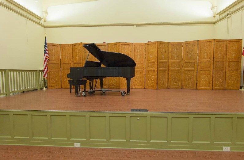 A grand piano on an empty stage in an auditorium.