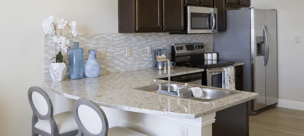 A modern kitchen with a marble countertop, stainless steel appliances, and decorative backsplash tiles.