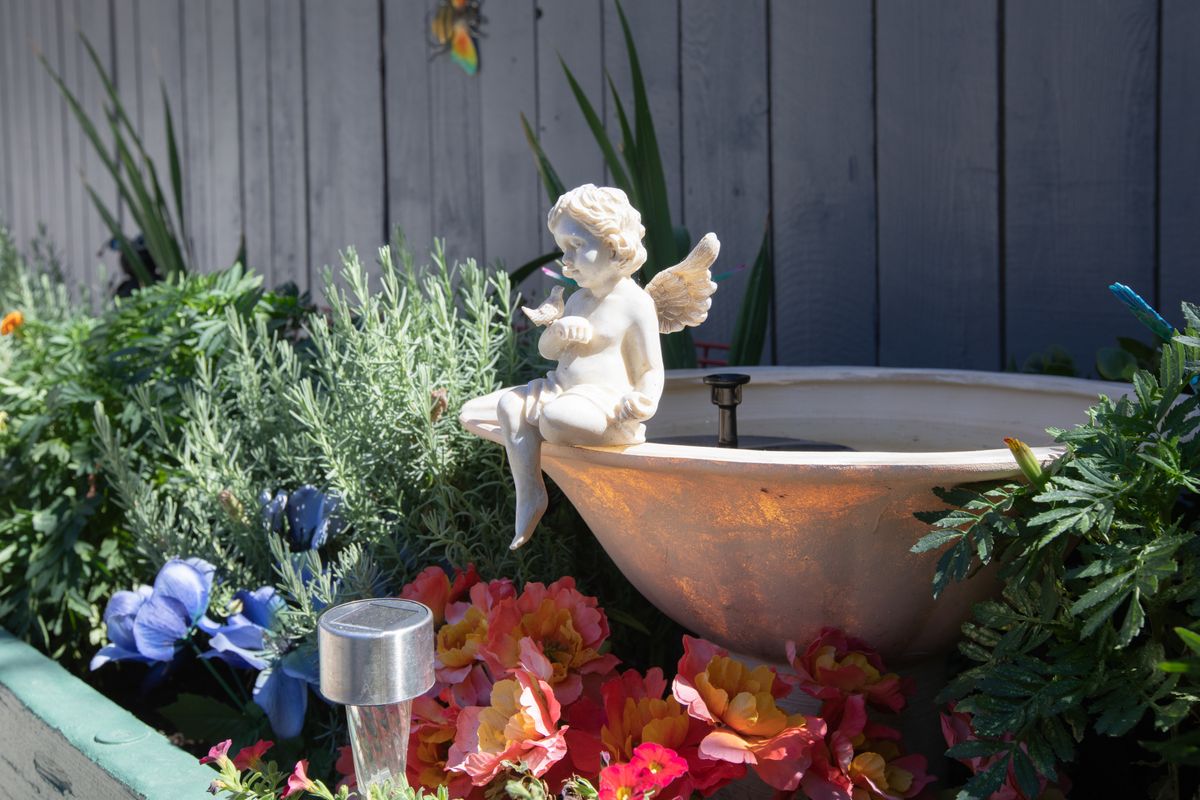 A serene garden scene with a cherubic angel statue sitting on a basin surrounded by colorful flowers.