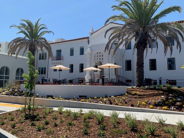 A sunny day view of a white building with palm trees and an outdoor seating area.