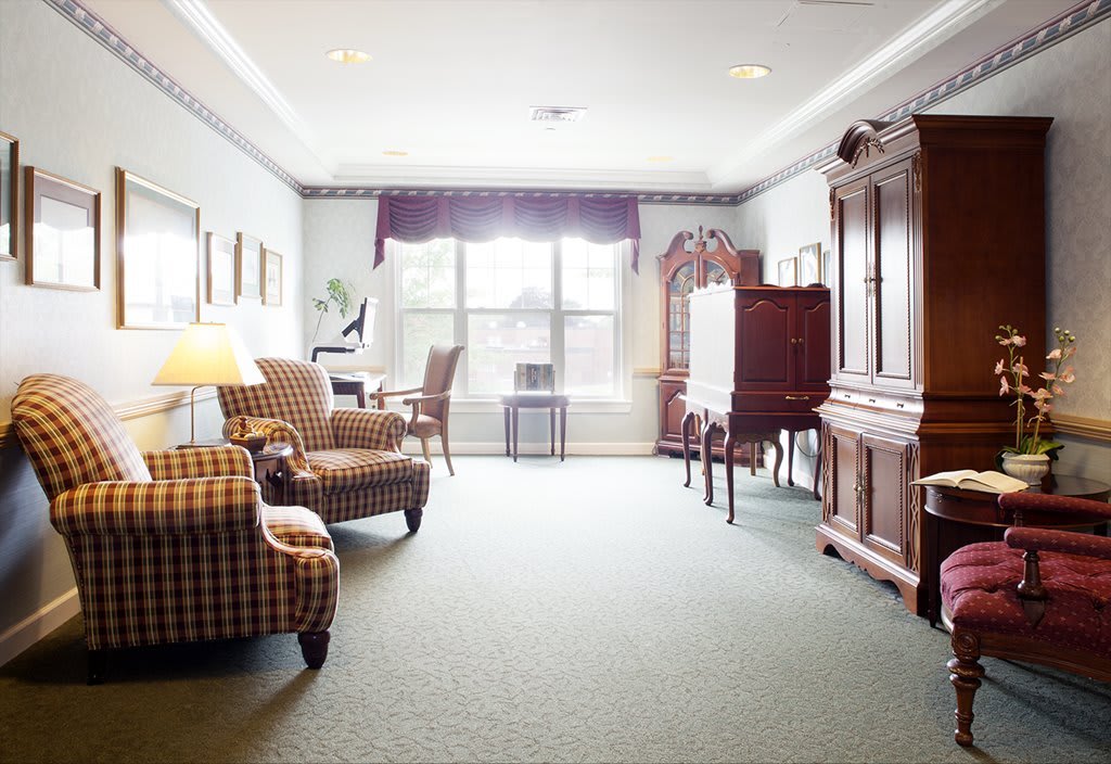 A cozy living room with armchairs and a large wooden cabinet, illuminated by natural light from the window.