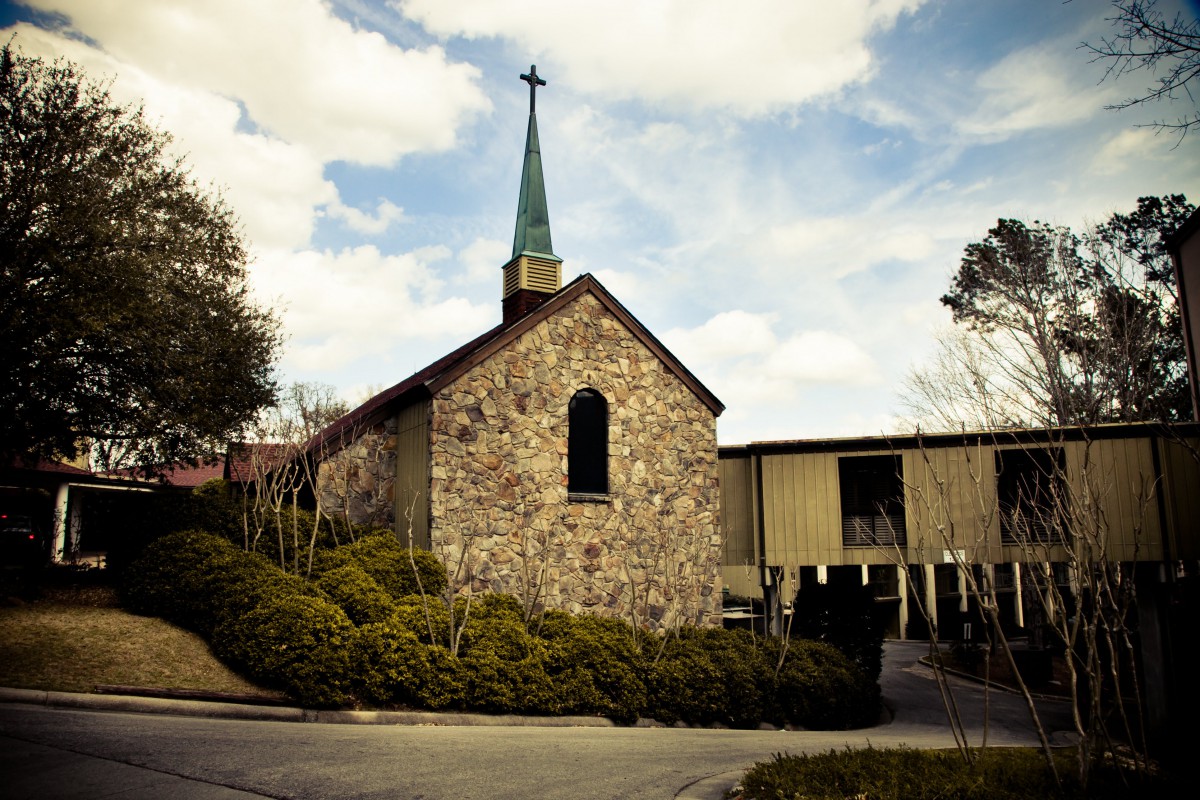 A stone church with a tall steeple set against a partly cloudy sky.