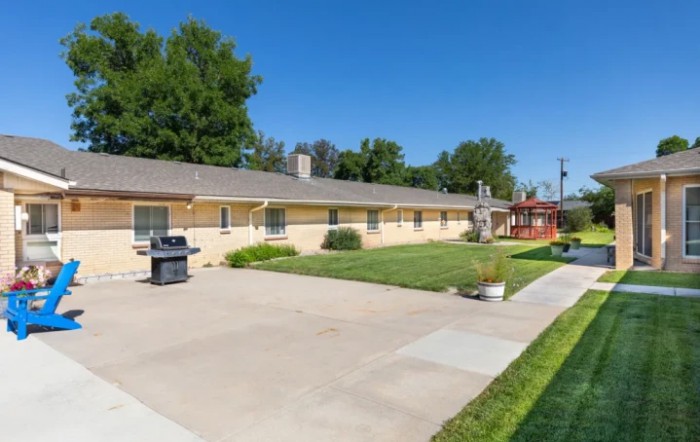 A single-story house with a neatly maintained lawn and driveway, featuring an outdoor grill.