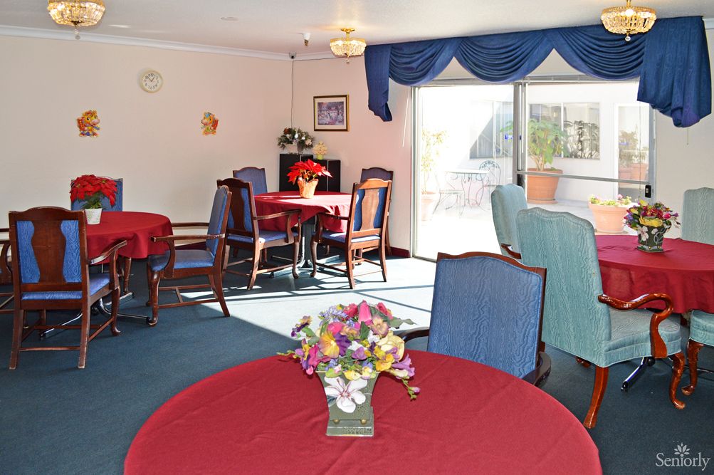 A cozy dining room with red tablecloths and blue chairs, featuring decorative flowers and ample natural light.