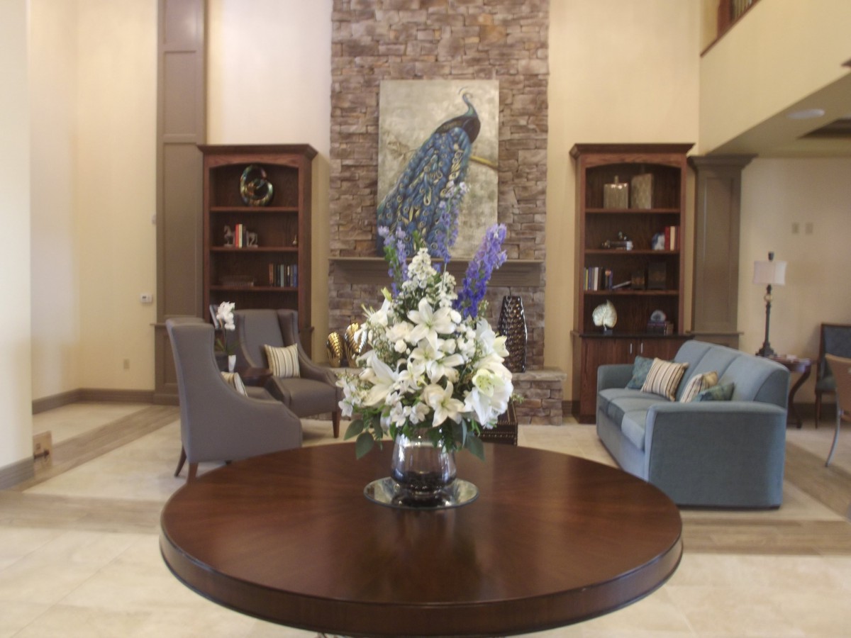 A beautifully decorated living room featuring a central table with a floral arrangement, surrounded by comfortable seating and adorned with a peacock artwork.