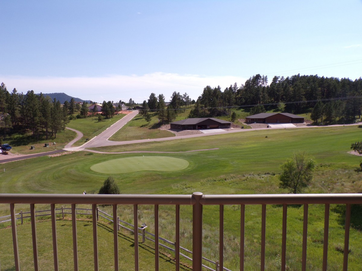 A scenic view of a golf course surrounded by trees and buildings under a clear, sunny sky.